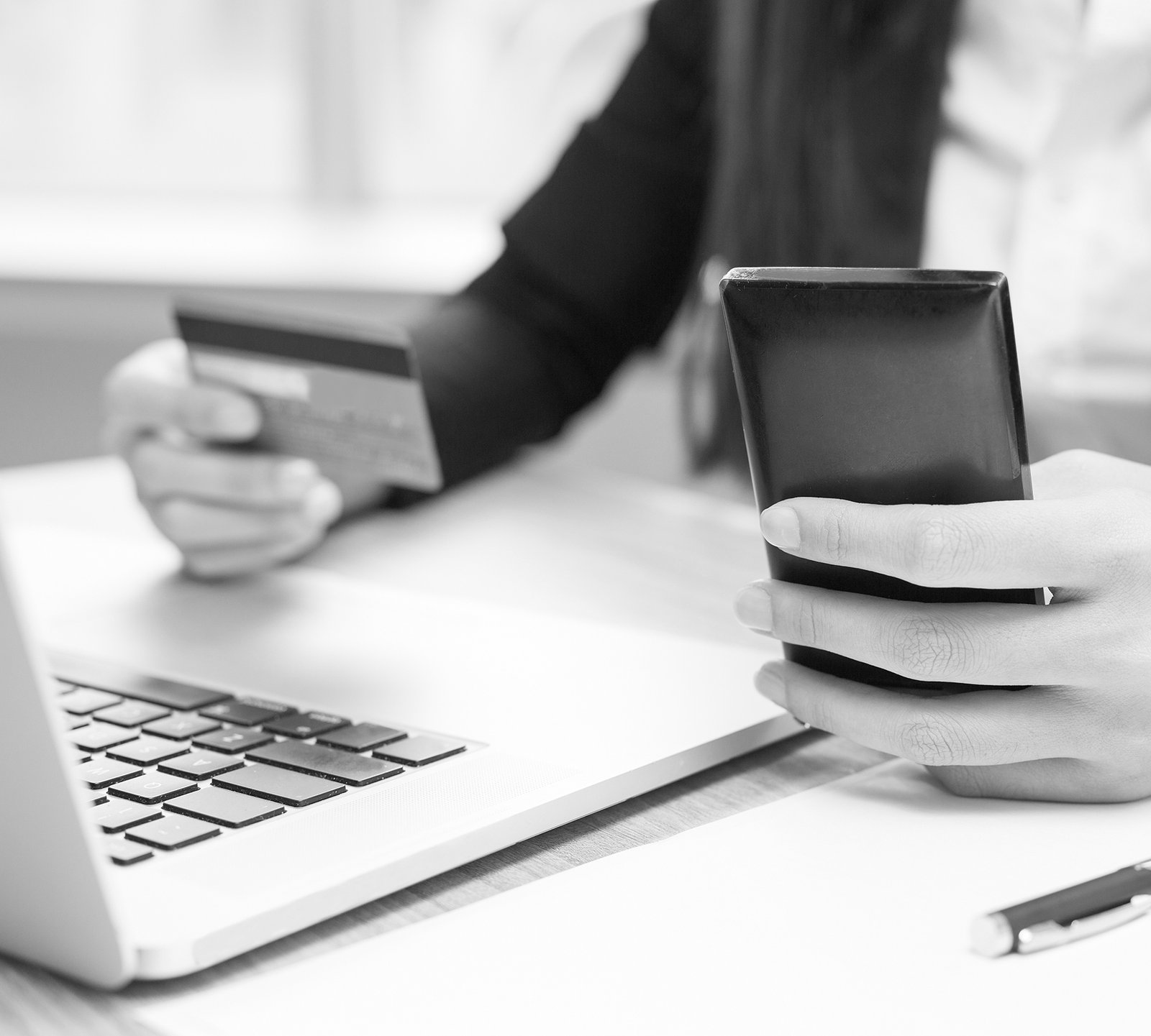 Cropped view of business woman working on laptop computer, holding credit card and smartphone and doing online banking at office desk